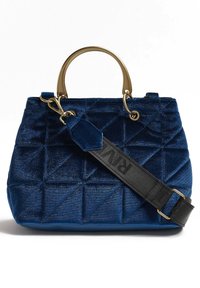 Sac à main en velours bleu avec un design matelassé, doté d'une anse circulaire dorée et d'une sangle noire amovible avec des lettres imprimées.