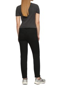 Czarne skinny jeans z średnim stanem, z dwoma tylnymi kieszeniami, zestawione z dopasowaną szaro-skalą koszulką i srebrnymi trampkami.