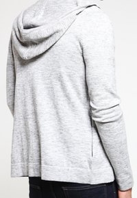 Heller grauer Kapuzenpullover aus weichem, strukturiertem Stoff. Verfügt über eine lässige Passform, lange Ärmel und seitliche Schlitze am Saum.