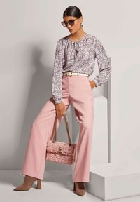 Helllila Paisley-Bluse mit gerafftem Ausschnitt, kombiniert mit hoch taillierten, blassrosa weit geschnittenen Hosen und einer strukturierten rosa Handtasche.