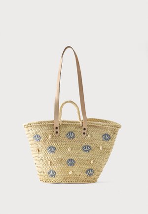 Sac cabas en paille tissée avec deux anses en cuir beige, décoré de motifs de coquillages bleus et de petites coquilles beiges.
