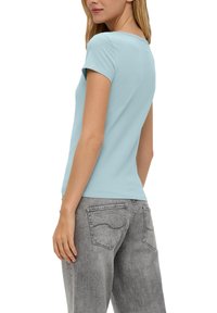 Helles blaues T-Shirt mit kurzen Ärmeln, rundem Ausschnitt und glatter Textur, kombiniert mit grauen, locker sitzenden Jeans mit Gesäßtaschen.