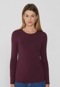 Langärmliges Rundhalsoberteil in tiefem Burgunderrot, aus weichem Material mit glatter Textur. Hat enganliegende Ärmel und ein schlichtes Design.
