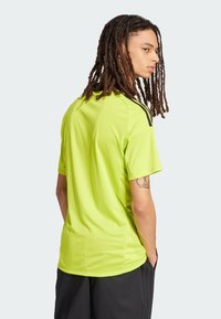 Camiseta deportiva de color verde neón con tejido texturizado, de manga corta y con acentos negros en los hombros, combinada con pantalones cortos negros.