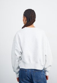 Sudadera gris de corte relajado, con costuras de hombro caídas y puños elásticos. Combinada con jeans azules, que destacan su diseño cómodo.