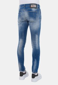 Verbleekte blauwe denim jeans met een slim fit, beschadigde details en een wit accentpatroon. Beschikt over een merkband en achterzakken.