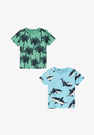 Two short-sleeve t-shirts: one green with black palm tree print, one light blue with black shark patterns, both cotton fabric.