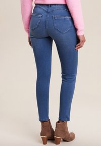 Jean bleu foncé à coupe slim, avec des poches arrière et une taille haute, associés à des bottines brunes à talon empilé.