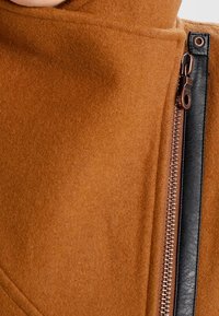 Braune Wollmischung Jacke mit hohem Kragen. Verfügt über einen schwarzen Reißverschluss an der Seite und hat eine glatte Textur, die ein schlankes Designmerkmal zeigt.