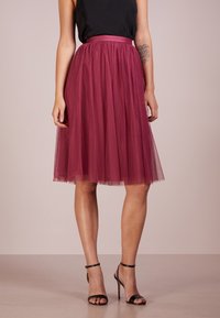 Burgundyröd tullekjol med prickmönster, hög midja och knälång längd. Matchad med svarta högklackade sandaler med remmar.