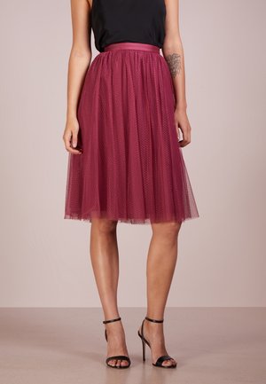 Falda de tul burdeos con un patrón de puntos, cinturilla alta y corte hasta la rodilla. Combinada con sandalias negras de tacón alto y tiras.