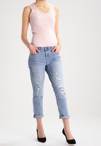 Rosa ribbad linne med spetsdetaljer, i kombination med ljusblå slitna jeans med fransar på fållen och svarta högklackade skor.