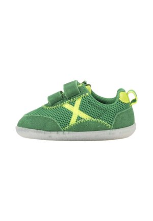 Zapatilla para niño pequeño en verde y amarillo con tejido de malla, dos tiras de velcro, una pestaña en el talón y una suela blanca flexible.
