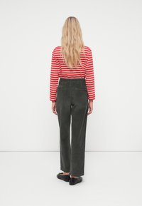Green corduroy trousers with wide-leg fit, paired with a red and white striped long-sleeve top. Back view shows waistline details and pockets.