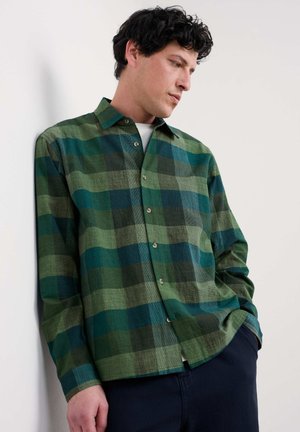 Green plaid shirt with a button-down collar, featuring varying shades of green and blue, made of textured fabric, worn over a white shirt.