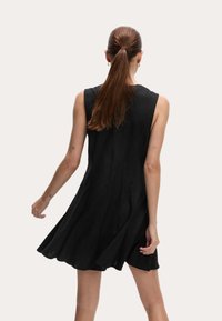 Abito senza maniche in lino nero con orlo svasato e pieghe posteriori, caratterizzato da una texture morbida e un design minimalista.