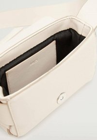 Pequeño bolso cruzado color crema con forro interior negro y cierre a presión magnético, que muestra un compartimento interno para tarjetas etiquetado como "MNG".