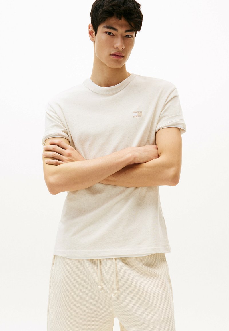 T-shirt a maniche corte di colore beige chiaro, realizzato in un tessuto morbido, con un piccolo logo ricamato sul petto, abbinato a pantaloni corti leggeri coordinati.
