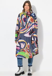 Impermeabile colorato con motivi astratti in rosso, arancio e verde su uno sfondo scuro, dotato di chiusura con zip e cappuccio.