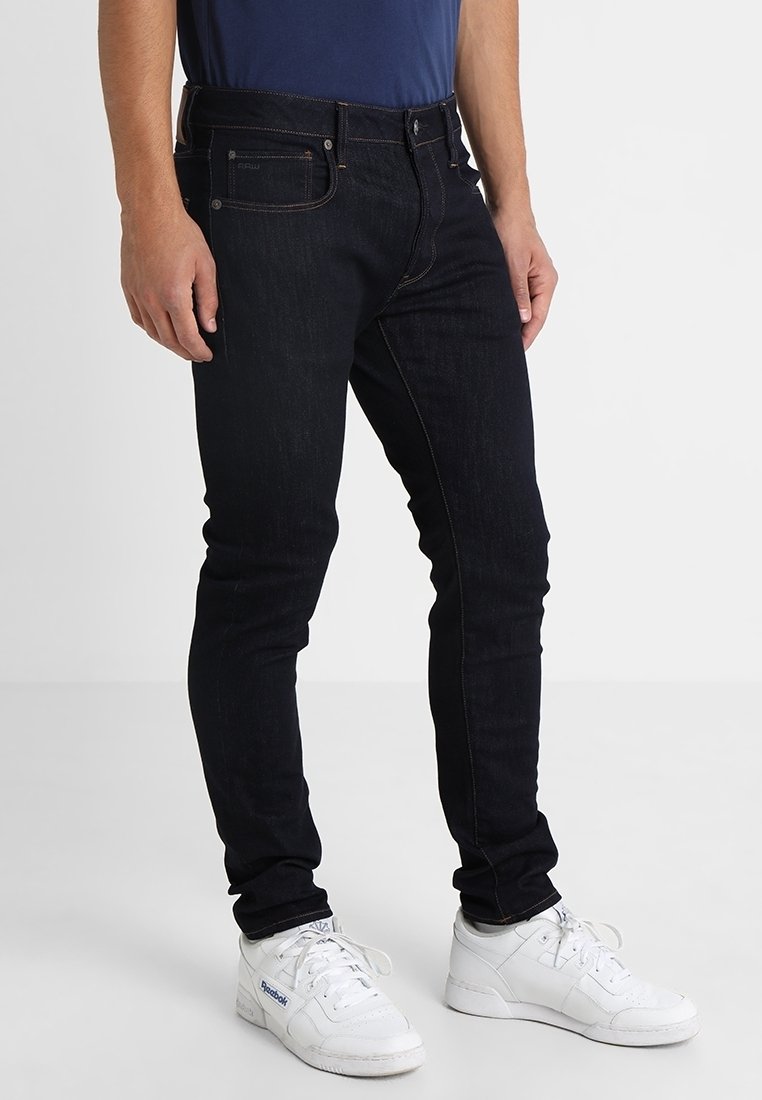 Tmavě modré džíny se slim fit střih, s kontrastním šitím a designem se pěti kapsami. Nosené s bílými teniskami.