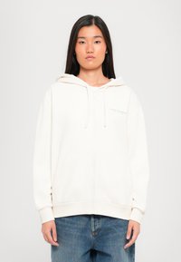 Lichtbeige zip-up hoodie met een trekkoordkapuchon, voorzakken en geribbelde manchetten. Bevat subtiele logo-opdruk op de borst.