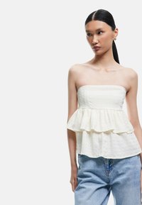 Top peplum blanco sin tirantes con tejido texturizado, que presenta un dobladillo acampanado y un diseño de volantes en capas, combinado con vaqueros de mezclilla azul claro.