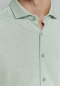 Lichtgroen shirt met korte mouwen en een zachte textuur, een kraag en bijpassende groene knopen, met een subtiele gemêleerde patroon.