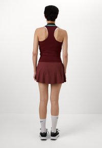 Débardeur bordeaux avec un design dos nageur et une jupe-culotte assortie. Présente un liseré turquoise au niveau du cou. Porté avec des chaussettes blanches et des baskets noires.