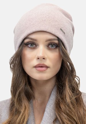 Lichtroze beanie muts met een geribbelde tekstuur, aansluitend ontwerp en een klein accentlogo. Gedragen over lang, golvend bruin haar.