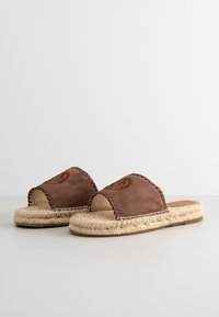 Brown suede slip-on sandals with woven jute soles. Features stitched detailing and a smooth texture. Open-toe design for breathability.