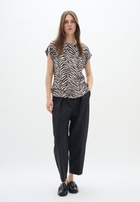 Top a maniche corte beige con strisce zebra nere, abbinato a pantaloni neri larghi e mocassini neri. Tessuto morbido, design casual.
