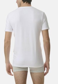 T-shirt bianco in cotone con maniche corte e scollo rotondo, indossato con pantaloni boxer grigi chiari, mostrando una superficie liscia e un design semplice.