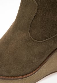 Stivale alla caviglia in camoscio verde oliva con punta arrotondata, caratterizzato da un delicato motivo cucito e una suola a zeppa testurizzata grigio chiaro.
