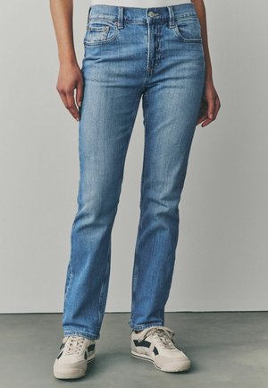 Helle blaujeans mit geradem Bein, Fünf-Taschen-Design, mit Metallknopf und Reißverschluss, kombiniert mit beigen Sneakern.