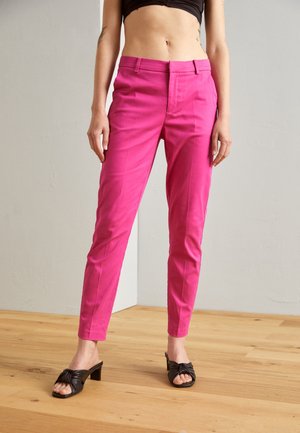 Fitted, high-waisted trousers in bright pink fabric with a smooth texture. Features front pockets and a tapered leg design. Paired with black knot-heel mules.