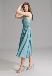 Aqua Chiffonkleid mit verziertem Oberteil, durchsichtigen Seiten und A-Linien-Rock. Abgerundet mit metallischen, geschlossenen High-Heelsandalen.