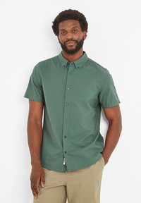Short-sleeve, button-up shirt in dark green fabric, featuring a classic collar, visible buttons, and a tag at the hem.