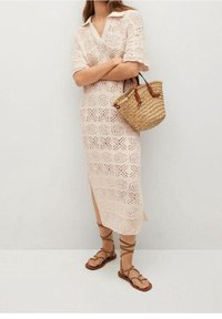 Robe tricotée, de couleur rose pâle, avec une texture à motifs et des manches courtes ; associée à un sac en paille tissé et des sandales à lanières marron.
