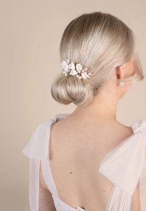 Haaraccessoire mit weißen Blumenmotiven und Perlendetails, platziert auf einem glatten blonden Dutt. Der Hintergrund ist hellbeige.