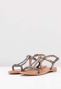 Metallische bronzen sandalen met een T-band ontwerp, platte zool en verstelbare enkelband. Getextureerde banden voegen visuele interesse toe.