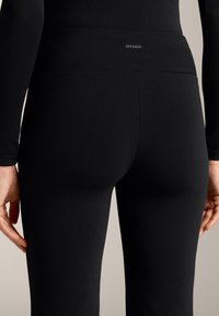 Čierne legíny vyrobené z elastického materiálu s vysokým pásom, na ktorom sa nachádza malé logo OYSHO. Hladký povrch a priliehavý dizajn.