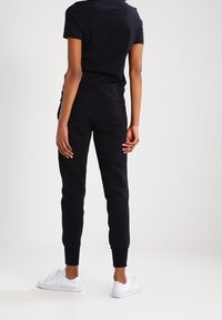 Svart bomullskorta med kort ärm i kombination med svarta tapered sweatpants, med ribbade mudd och vita sneakers.