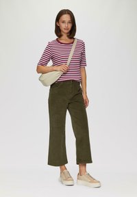 Pasiasta burgundowa i biała koszulka z krótkim rękawem, oliwkowe szerokie spodnie i beżowe trampki. Modelka trzyma torebkę na ramię w kremowym kolorze.