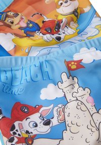 Costumi da bagno per bambini con vivaci design di cartoni animati. Tessuto blu con adorabili cuccioli, castelli di sabbia e il testo "TEMPO DI SPIAGGIA". Texture liscia.