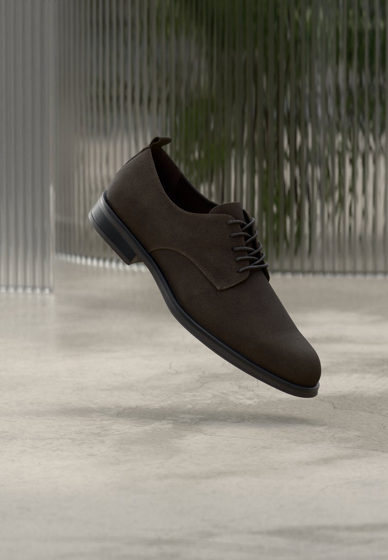 Καφέ οξφορντ παπούτσι από σουέντ με λεία υφή, στρογγυλεμένη μύτη και σχέδιο με κορδόνια. Διαθέτει μαύρη καουτσούκ σόλα και διακριτικό τακούνι.
