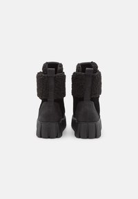 Botas negras hasta el tobillo con suela gruesa, con un collar de piel texturizada y cuerpo de ante suave. Incluyen una pestaña trasera para facilitar su uso.