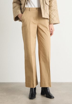 Tan wide-leg trousers made from a smooth fabric, featuring a tailored fit, front pockets, and a classic button closure. Paired with black heeled boots.
