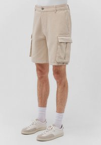 Beige Cargo-Shorts mit zwei seitlichen Taschen, einer Klappentasche am Oberschenkel und einer geraden Passform. Hergestellt aus atmungsaktivem Baumwollstoff.