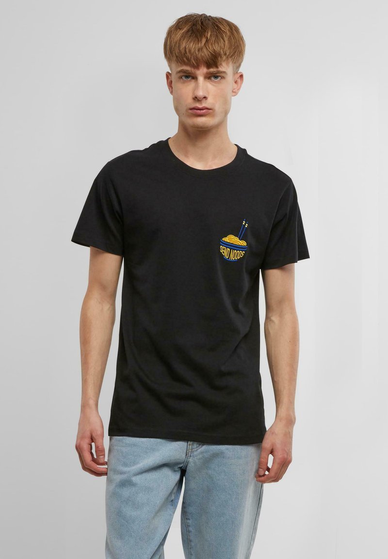 T-shirt en coton noir à manches courtes. Il présente un graphique d'un bol de nouilles jaune avec des baguettes sur la zone de la poitrine à gauche.