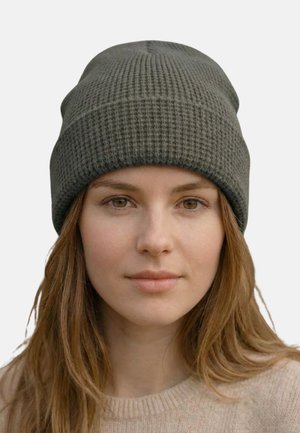 Woman with light brown hair wearing a textured dark gray beanie and a beige sweater, facing forward with a neutral expression.